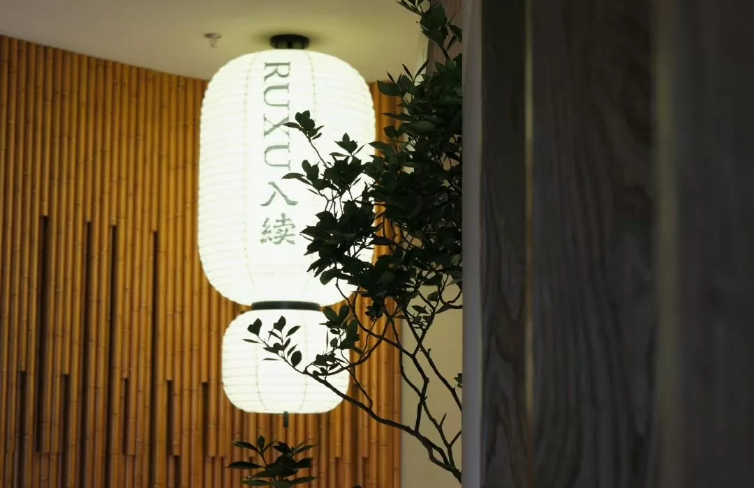 Illuminated RUXU rice-paper lantern against a bamboo wall