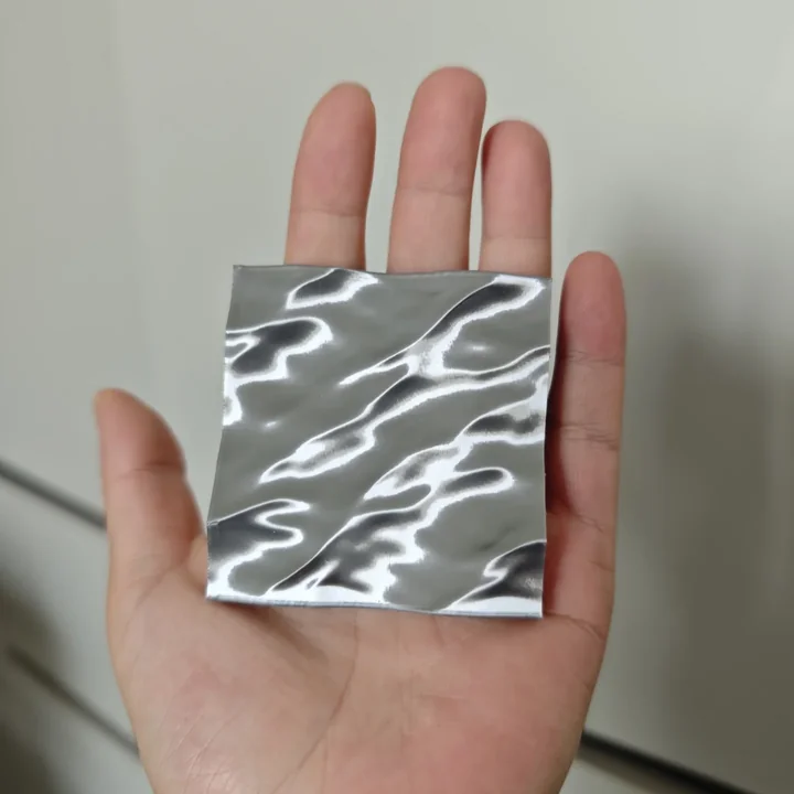 Hand-held reflective metal finish sample with a rippled surface